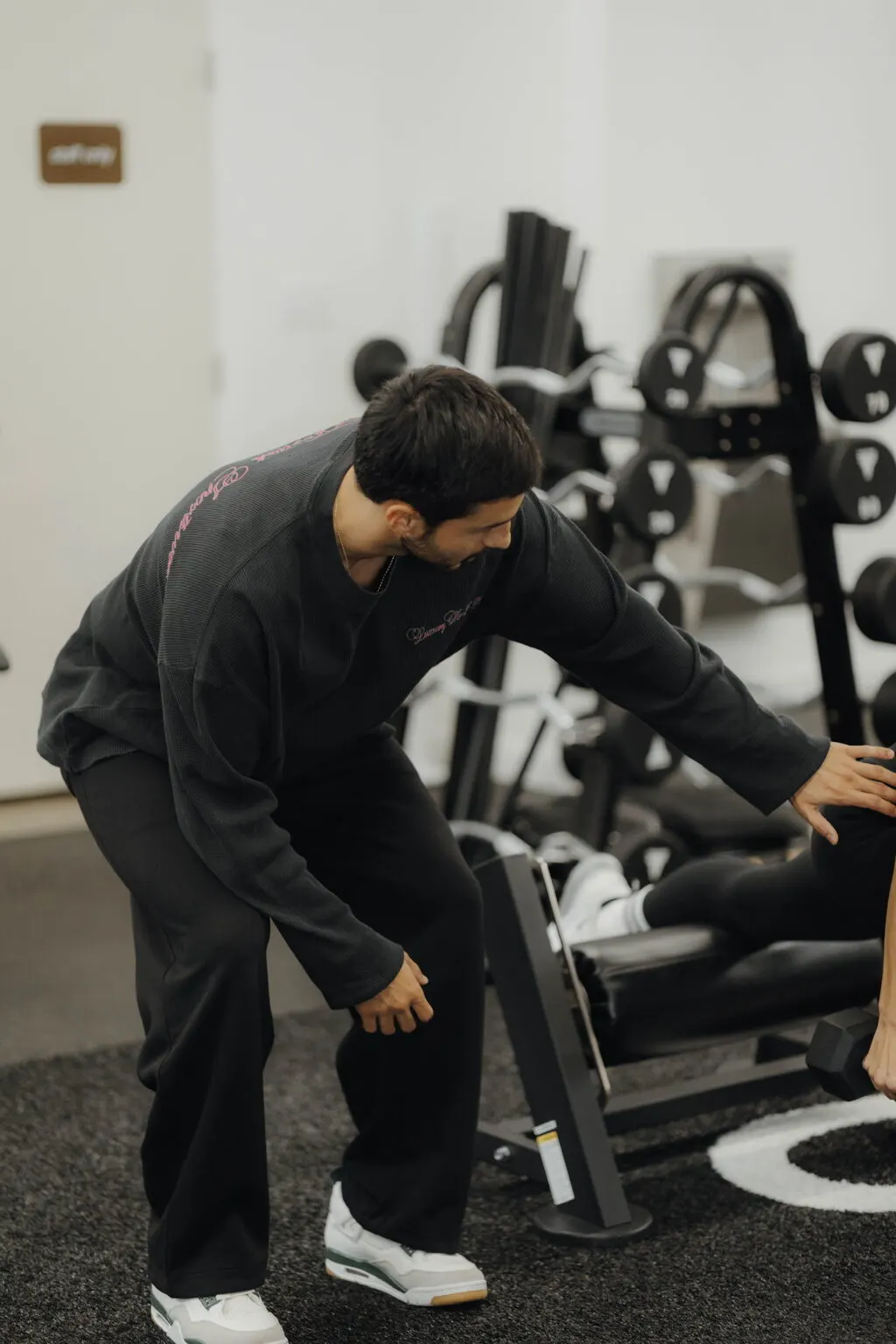 Coach Santi leaning in to adjust a client's setup on a machine at Focus Athletics, the close coaching that carries into small group training in Costa Mesa